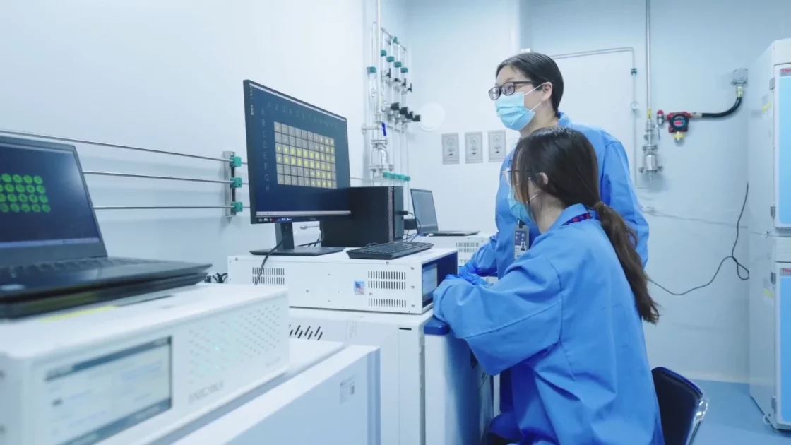 Two scientists in blue lab coats analyzing data from a high-content screening experiment displayed on computer monitors.