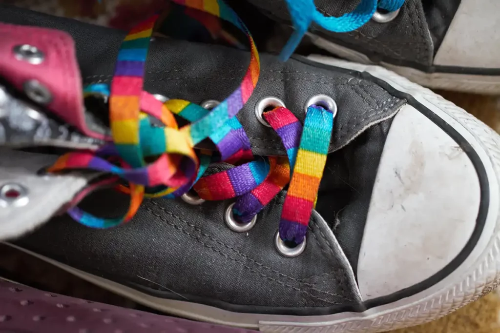 Close-up of worn black sneakers with bright rainbow laces tied loosely, symbolizing support for the Rainbow Laces Project.