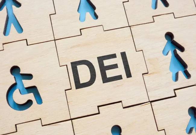Wooden puzzle pieces featuring icons representing diversity and inclusion, with the word "DEI" centered in bold black text.