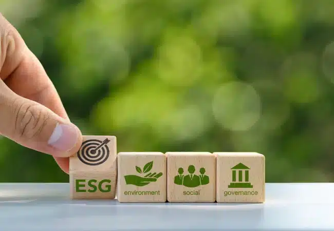 Hand arranging wooden blocks labeled ESG, environment, social, and governance, against a blurred green background symbolizing sustainability.