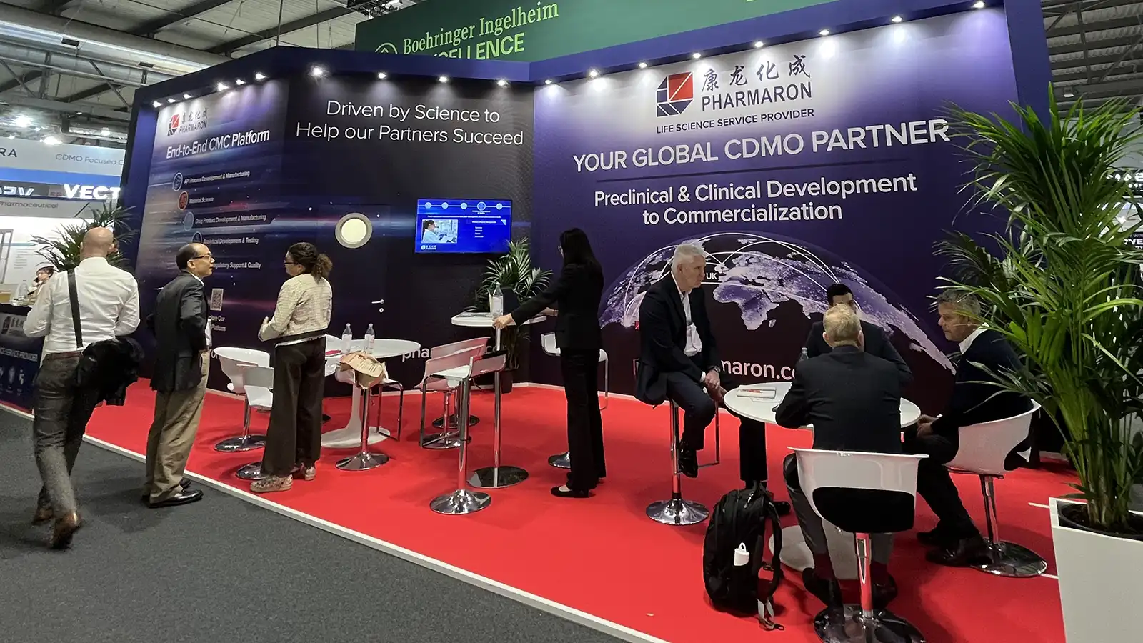 Pharmaron's trade show booth highlighting its CDMO and CMC services, with attendees networking and discussing preclinical and clinical solutions.