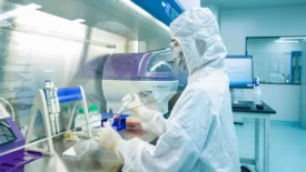 A scientist in full protective gear performs precise pipetting in a sterile lab environment, supporting advanced cell line development services (CLD).