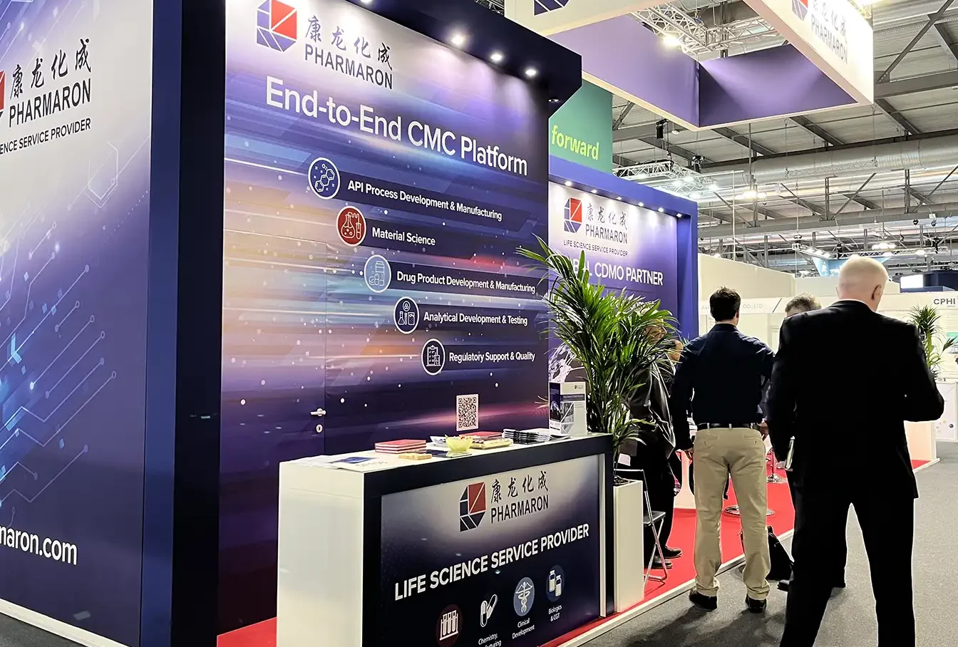 Exhibition booth showcasing Pharmaron's End-to-End CMC Platform with branded signage, informational displays, and attendees walking by.