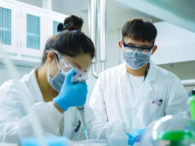 Scientists in a laboratory performing drug product development tasks with pipettes, safety goggles, and masks, ensuring precision and compliance.