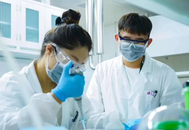 Scientists in a laboratory performing drug product development tasks with pipettes, safety goggles, and masks, ensuring precision and compliance.
