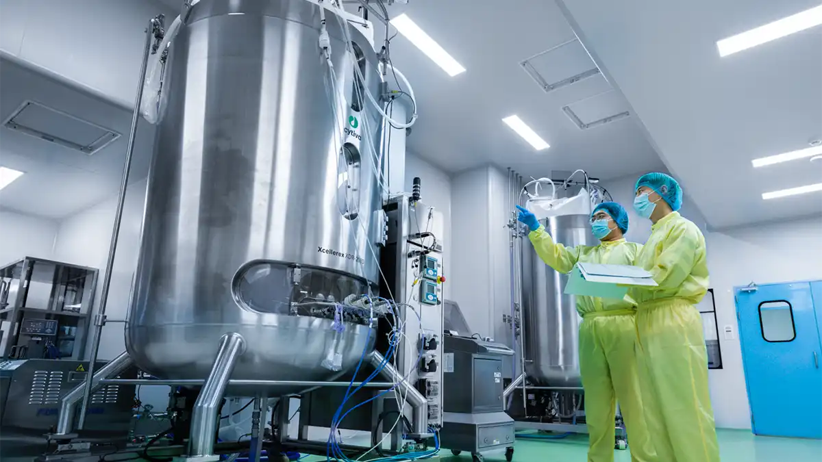 Scientists in protective gear oversee large bioreactors in a cleanroom, ensuring compliance with GMP standards for drug substance manufacturing.