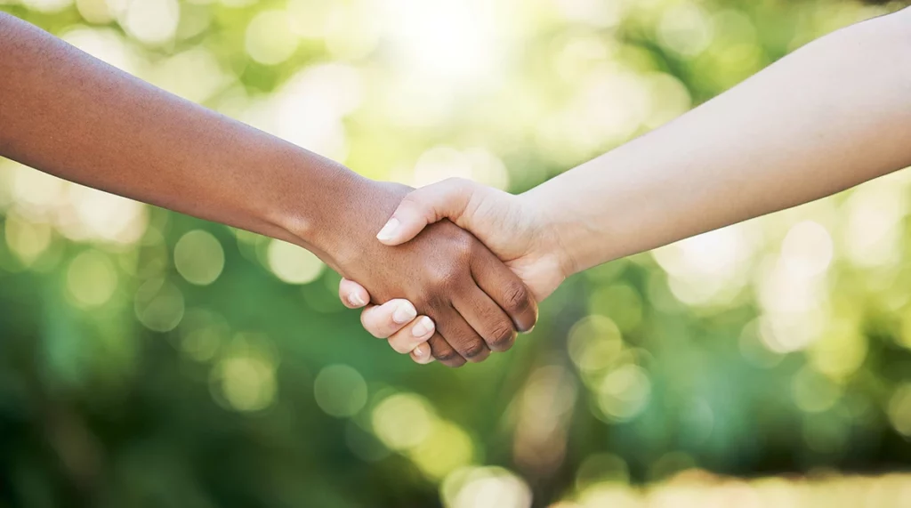 Two hands of different skin tones shaking firmly against a blurred green background, symbolizing unity and collaboration.