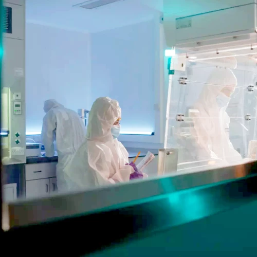 Scientists in full protective gear work in a dimly lit lab, focusing on oligonucleotides, radiolabeling, and metabolism studies within a sterile environment.