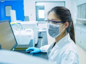 A scientist wearing protective gear works on a computer in a lab, supporting precise analytical services for research and development.