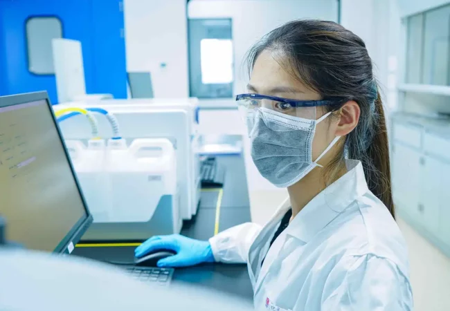 A scientist wearing protective gear works on a computer in a lab, supporting precise analytical services for research and development.