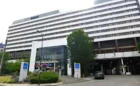 Exterior view of the Novotel London West, featuring a modern multi-story building with glass entryway, flags, and landscaped greenery.