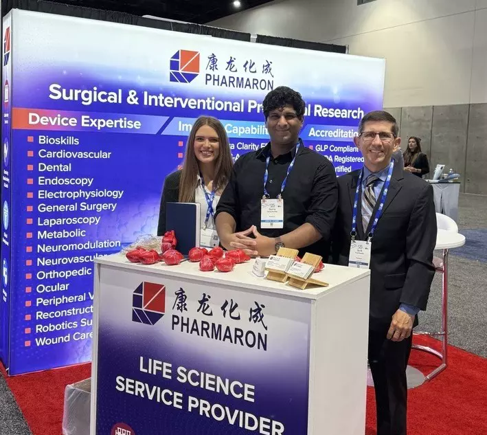 Three Pharmaron team members stand at a trade show booth promoting surgical and interventional preclinical research services and device expertise.