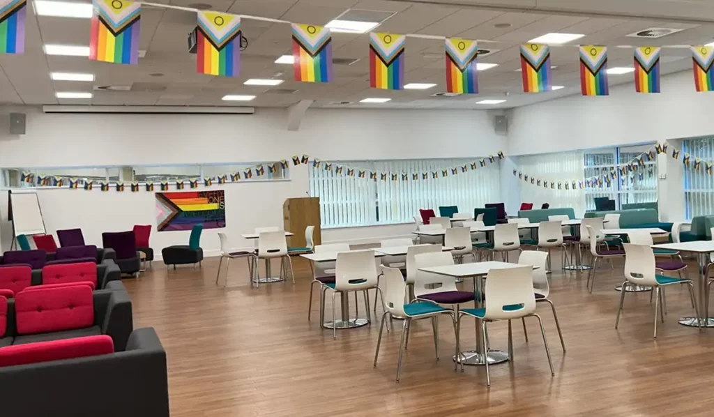 Spacious lunchroom decorated with PrideConnect flags, inclusive rainbow banners, and modern seating in vibrant, diverse colors.